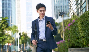 Young Asian Businessman Looking At Messages On Cellphone While Walking